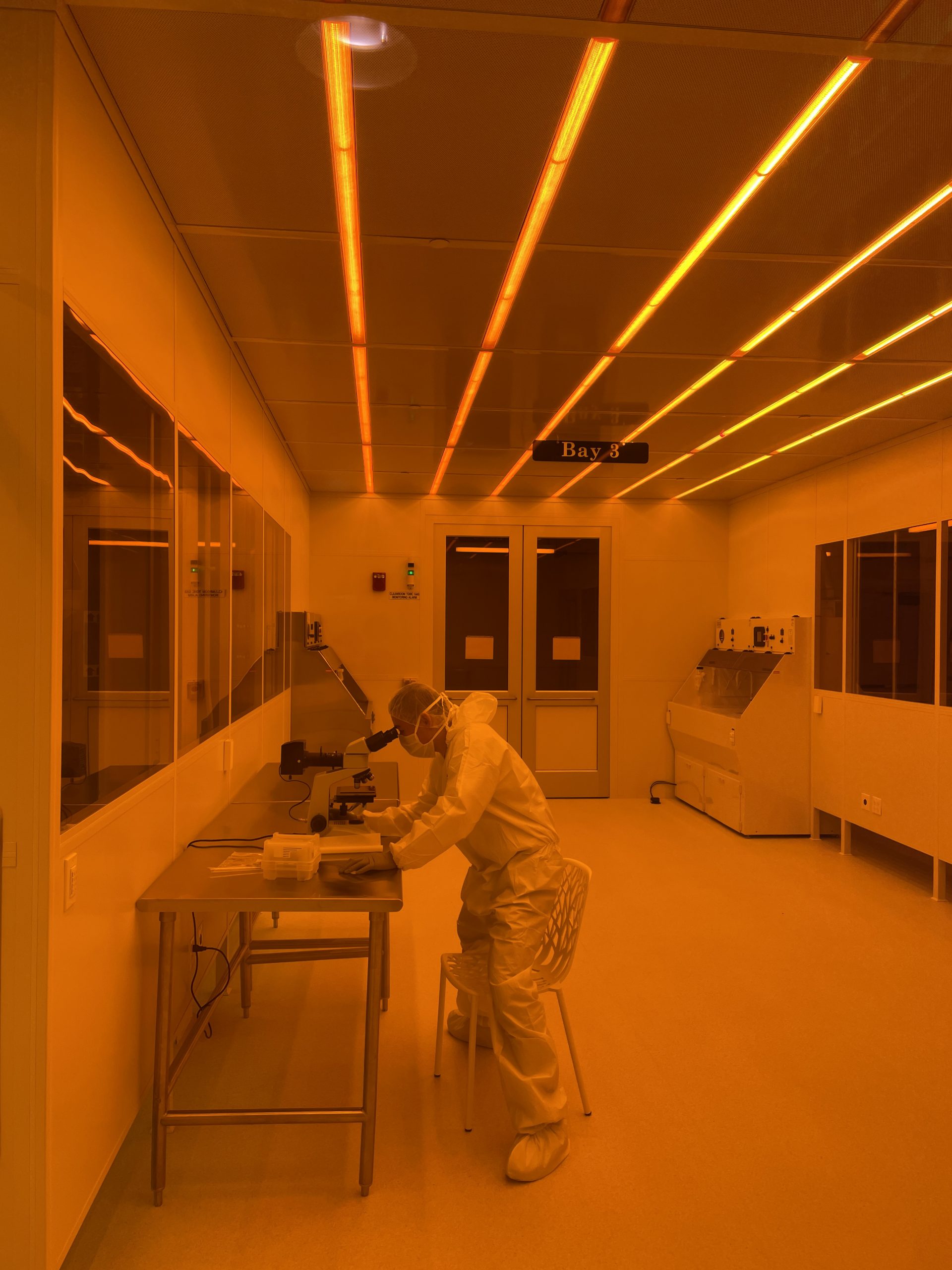 person working at binocular microscope in cleanroom bay 3